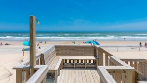 Une terrasse en bois donnant sur la plage, avec vue sur l’océan et les personnes qui se promènent sur la plage.