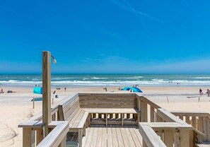 Een houten terras aan het strand met uitzicht op de oceaan en mensen op het strand.