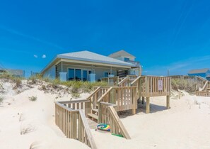 Een pand aan het strand met een houten terras, een strandbal en een helderblauwe lucht.