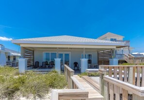 Een huis aan het strand met een overdekte veranda, buitenmeubels en een houten terras.