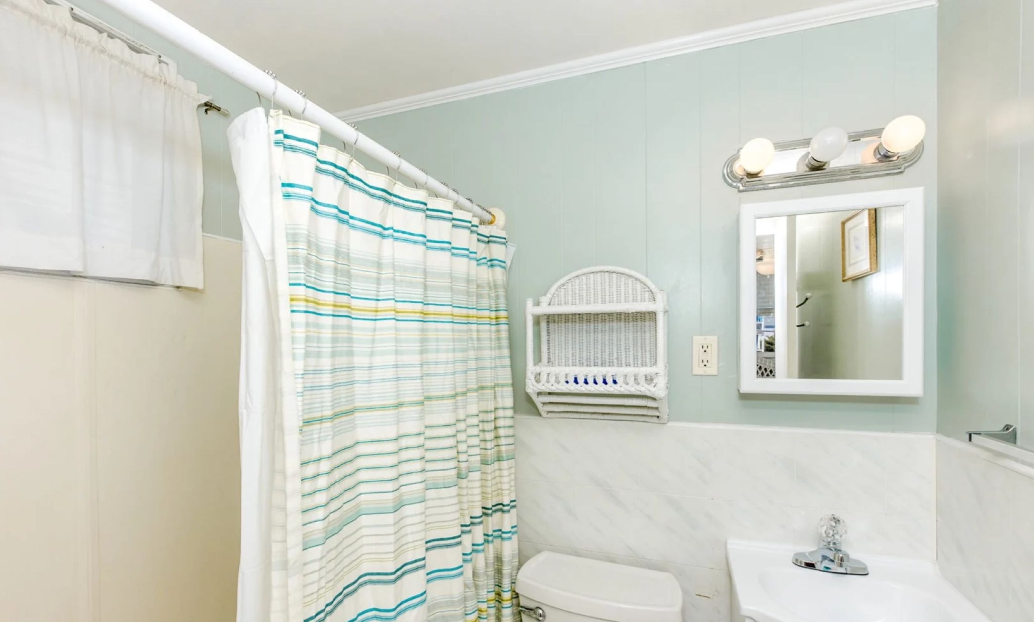 A bathroom with a striped shower curtain, a white sink, and a mirror with lights above it.