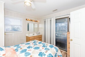 Un dormitorio con cama, tocador con espejo y puerta corrediza de vidrio que da a un balcón.