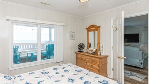Une chambre à coucher comprenant un lit, une commode, un miroir et donnant sur un balcon avec des chaises.