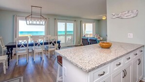 A spacious kitchen with a large island, white cabinetry, and a view of the ocean through the sliding glass doors. - Chez Nous - Classic 3BR Oceanfront Home with Modern Updates (Surf City)