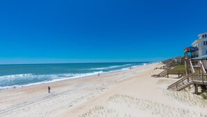 A beach with a building featuring a staircase leading to a deck. - Chez Nous - Classic 3BR Oceanfront Home with Modern Updates (Surf City)