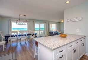 A spacious kitchen with a large island, a dining area with a view of the ocean, and a living area with a ceiling light fixture. - Chez Nous - Classic 3BR Oceanfront Home with Modern Updates (Surf City)