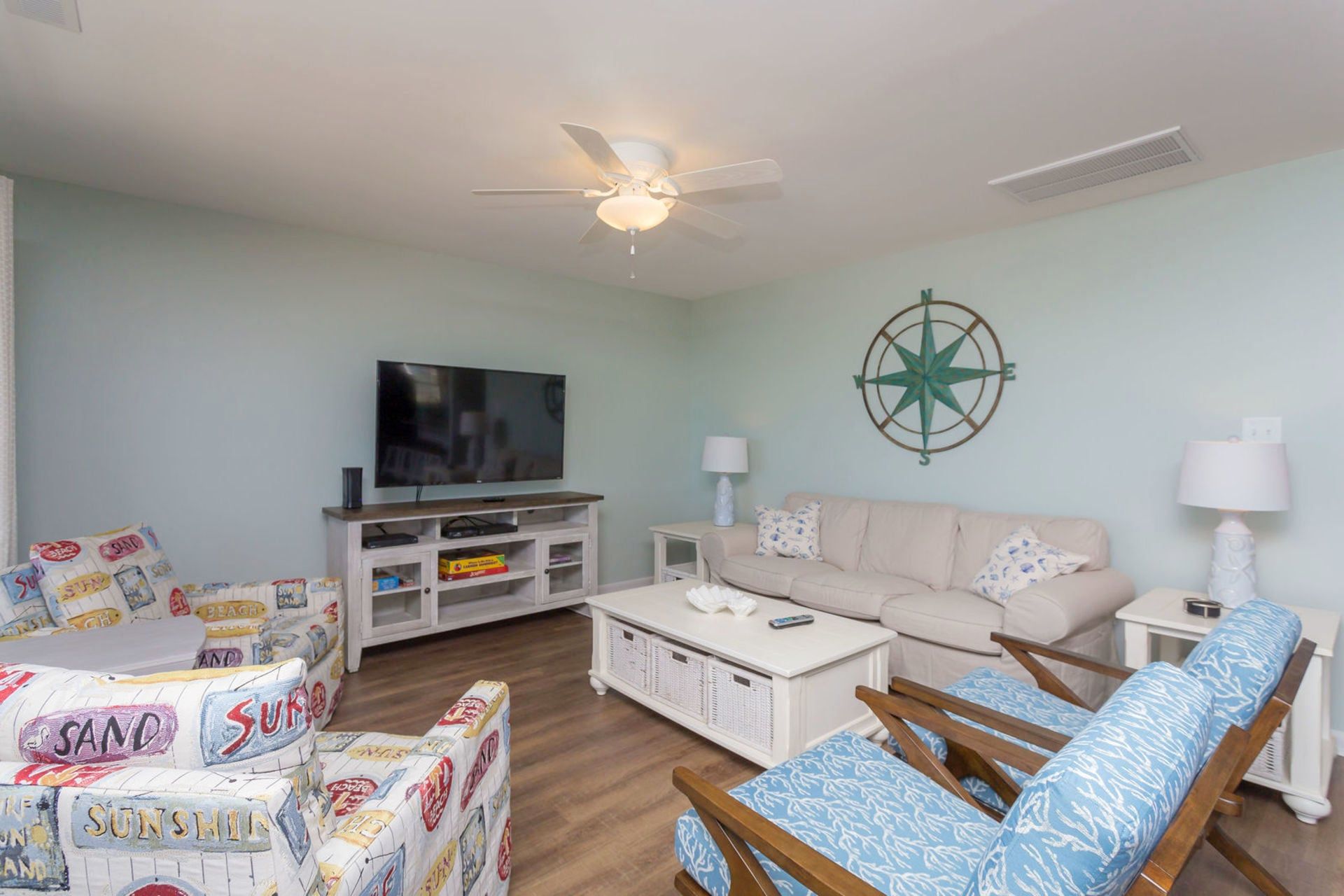 Ein Wohnzimmer mit Flachbildfernseher, Deckenventilator, Wandkompass und einer Couch mit gemusterten Kissen.