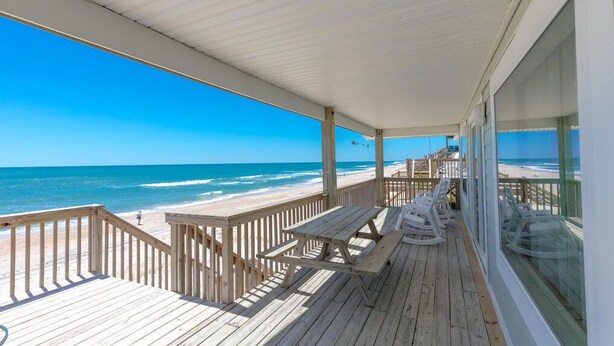 A wooden deck with picnic tables and chairs overlooking a beach. - Chez Nous - Classic 3BR Oceanfront Home with Modern Updates (Surf City)