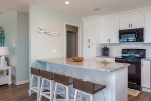 A kitchen with white cabinets, a granite countertop, a microwave, an oven, and a wooden island with bar stools. - Chez Nous - Classic 3BR Oceanfront Home with Modern Updates (Surf City)