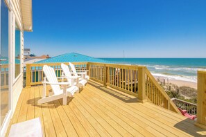 Une terrasse en bois avec des chaises blanches, une vue sur l’océan et un ciel dégagé.