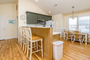 Une cuisine avec un îlot central, des chaises en bois, une table à manger et une poubelle.