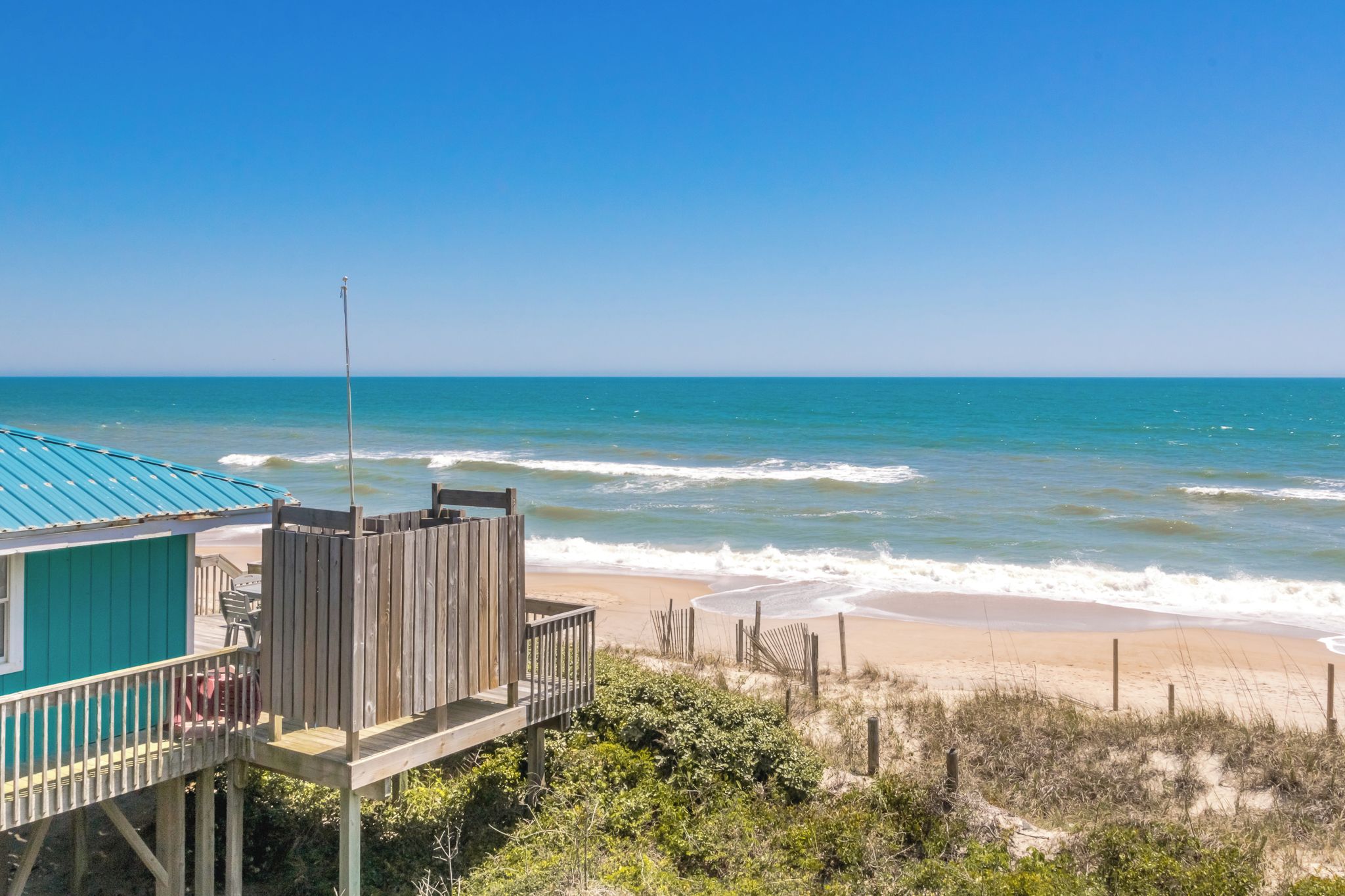 A beach house with a wooden deck and a view of the ocean.
