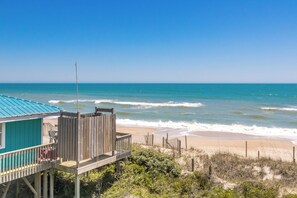 Une maison de plage dotée d’une terrasse en bois et offrant une vue sur l’océan.