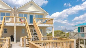 Une propriété située en bord de mer, comprenant un bâtiment à deux étages, une terrasse en bois et un escalier menant à l’étage supérieur.