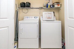 Une buanderie équipée de deux machines à laver blanches, d’un sèche-linge et d’une étagère contenant des produits de nettoyage.