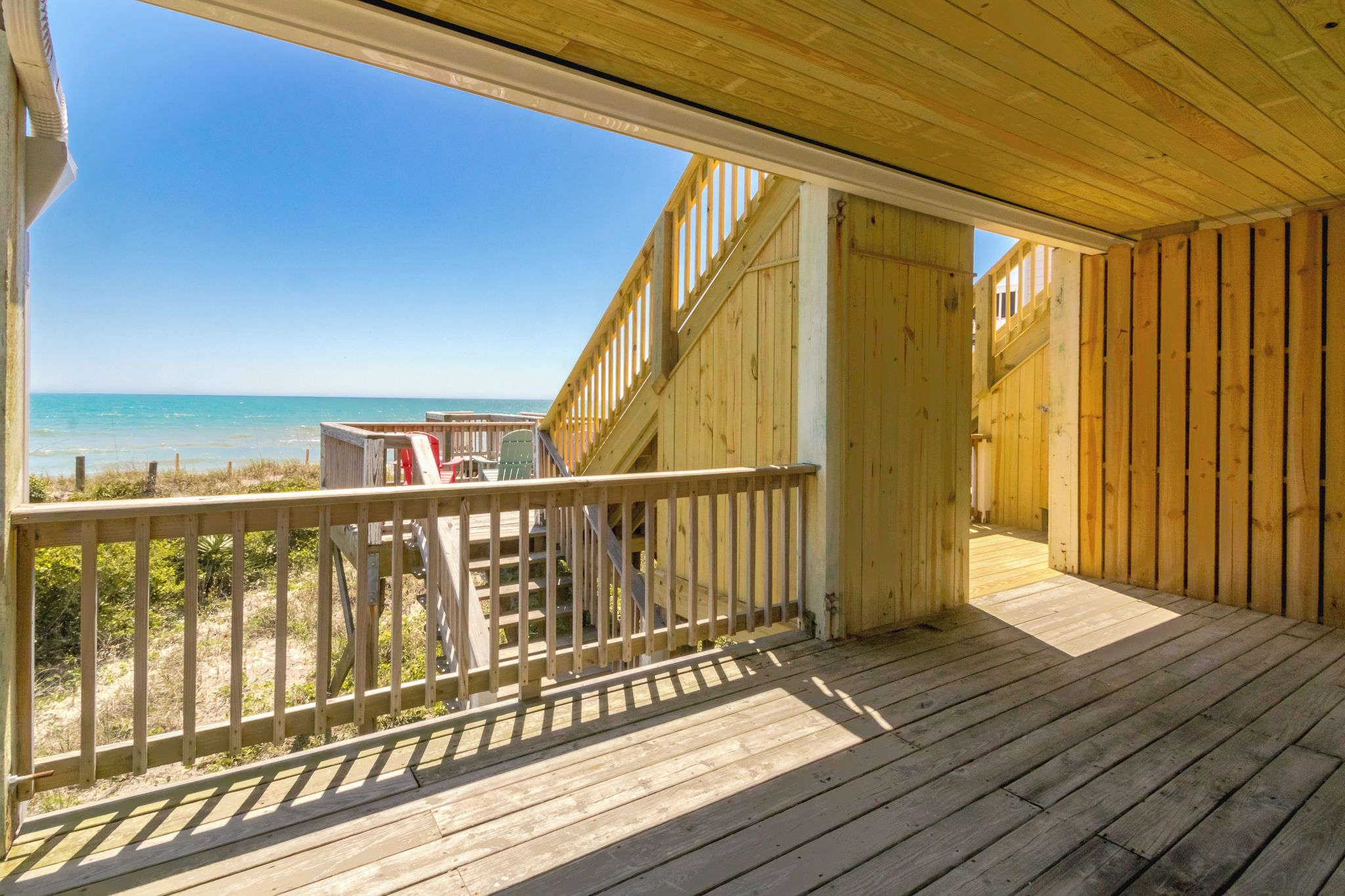 A wooden deck with a view of the ocean, a staircase, and outdoor seating.