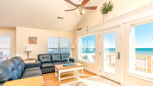 A living room with a black leather sofa, a wooden coffee table, and a view of the ocean through large sliding glass doors. - Dakota Dunes - Oceanfront!  Dog Friendly! (Surf City)