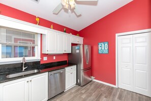 A kitchen with white cabinets, a stainless steel refrigerator, and a red accent wall. - Double U Seas - Oceanfront, Dog & Cat Friendly! (Surf City)