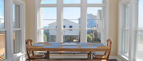 A dining area with a wooden table and benches, large windows, and a view of neighboring houses.