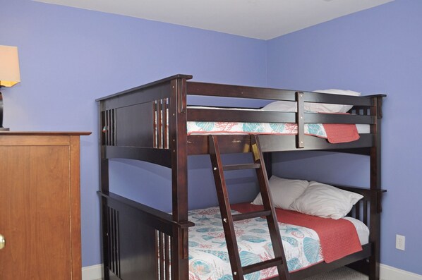 A bunk bed with a ladder, a wooden desk, and a wall socket.