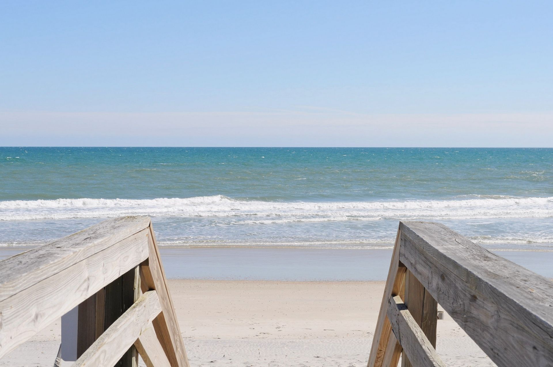 A wooden beach boardwalk leading to a sandy beach with the ocean in the background.