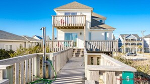 A beachfront property with a wooden deck leading to a two-story house with a balcony. - Fair Winds - Oceanfront (Surf City)