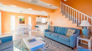 A bright living room with a blue sofa, white coffee table, and a staircase with white railings. - Fair Winds - Oceanfront (Surf City)