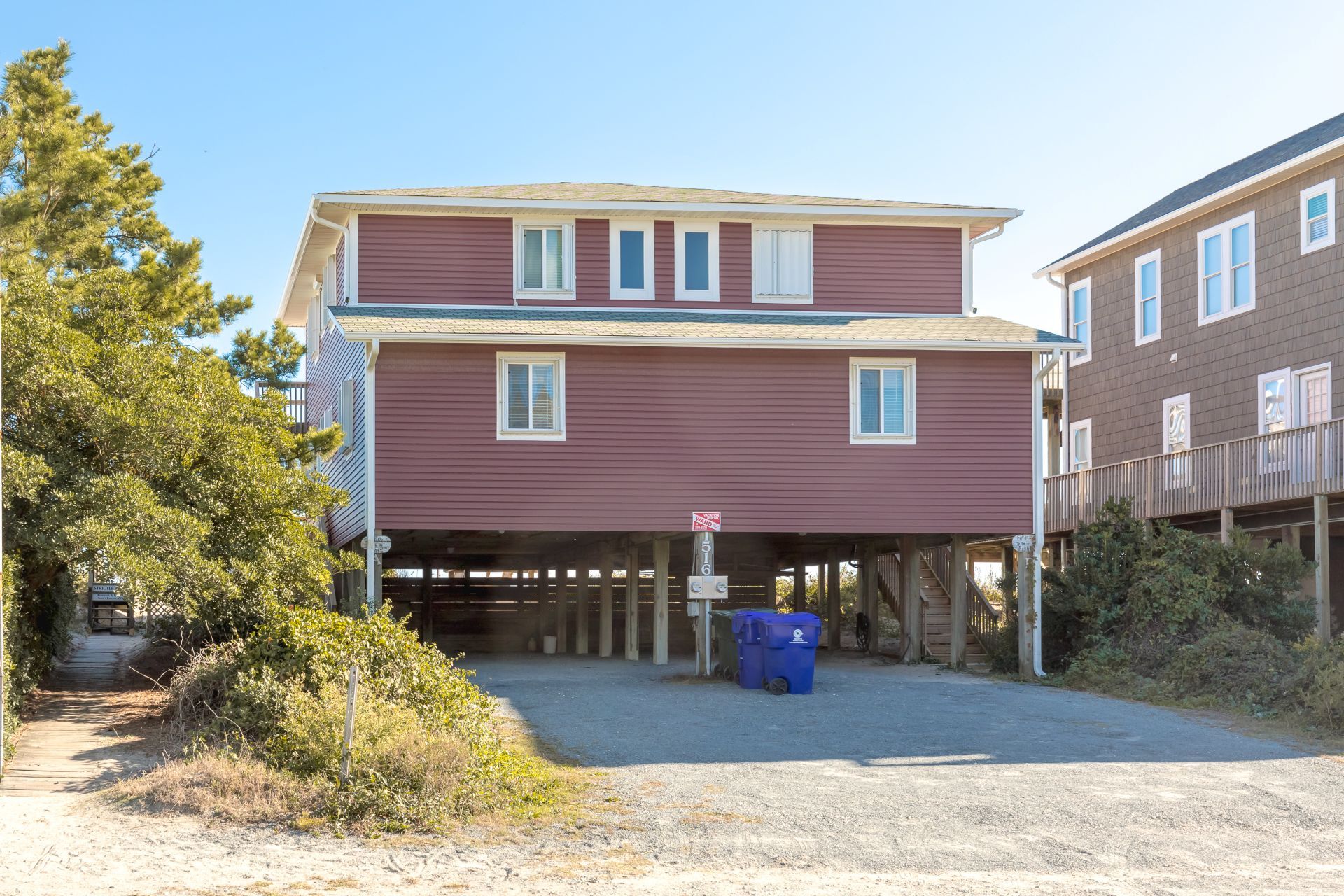 A two-story building with a covered parking area and a blue trash bin.