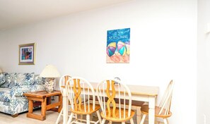 A living room with a sofa, a table, and chairs. There is a framed picture on the wall and a poster.