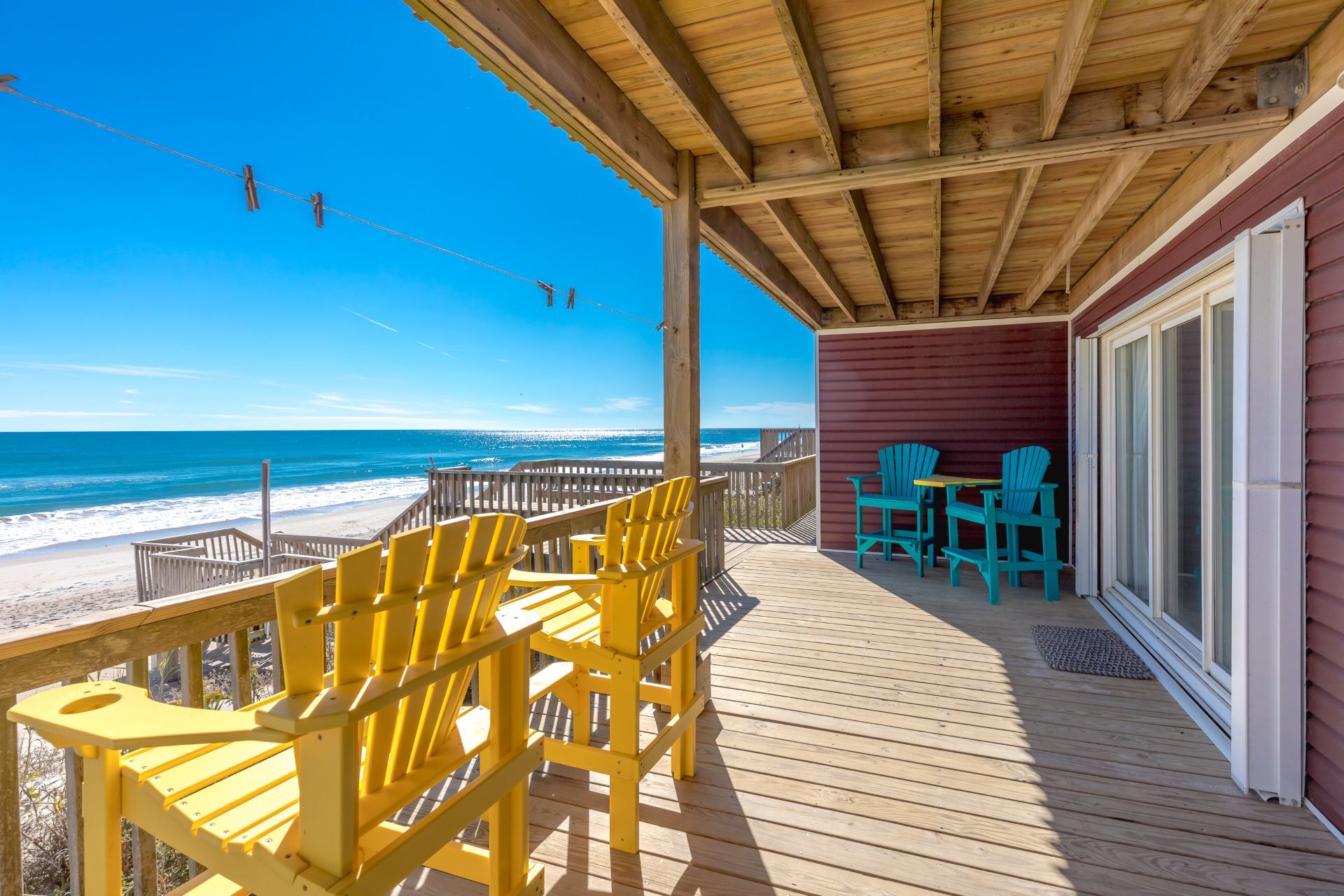 Eine Holzterrasse mit gelben Stühlen und einem Tisch mit Blick auf einen Strand und den Ozean.