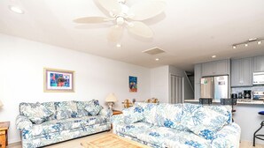 A living room with two sofas, a ceiling fan, and a kitchen area with cabinets and appliances. - Fins To The Left -Oceanfront 3 BR. (Surf City)