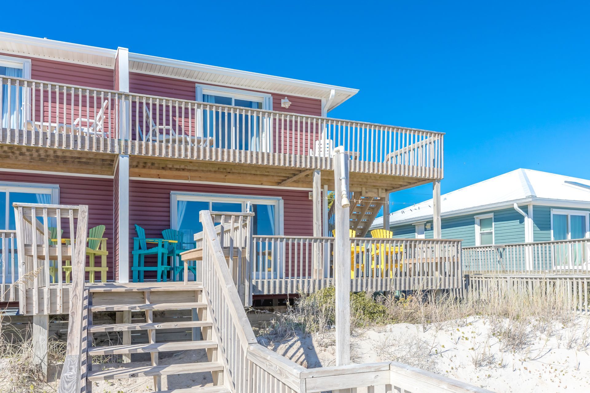 A multi-story beachfront property with a wooden staircase leading to a balcony.