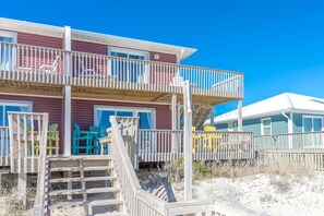 A multi-story beachfront property with a wooden staircase leading to a balcony, outdoor seating, and a clear view of the ocean. - Fins To The Left -Oceanfront 3 BR. (Surf City)