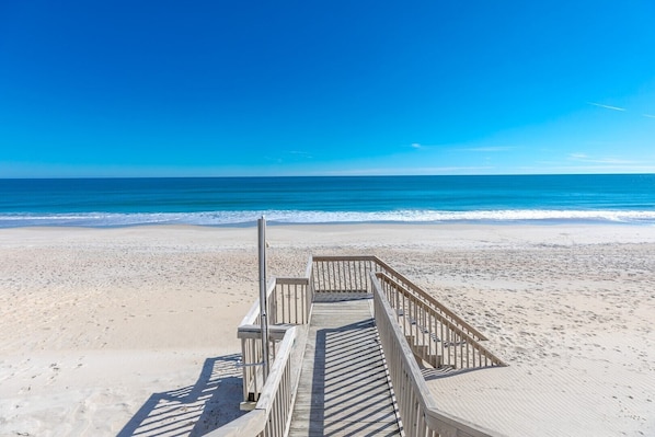 A wooden boardwalk leading to a beach with clear blue water and a sandy shore.