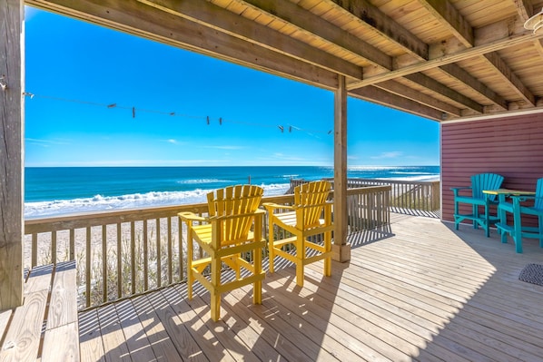 A wooden deck with chairs overlooking a beach.