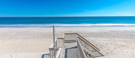 Ein hölzerner Steg führt zu einem Strand, bewölkter, klarblauer Himmel.