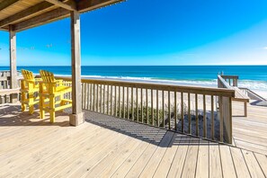 A wooden deck with a railing, yellow chairs, and a view of the ocean.