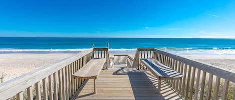 A wooden boardwalk leading to a beach with two benches.