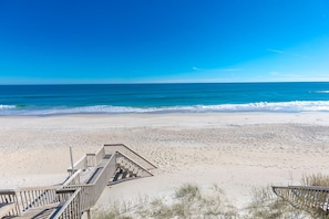 A beach with a wooden staircase leading down to the sand, a clear blue sky, and the ocean in the background.
