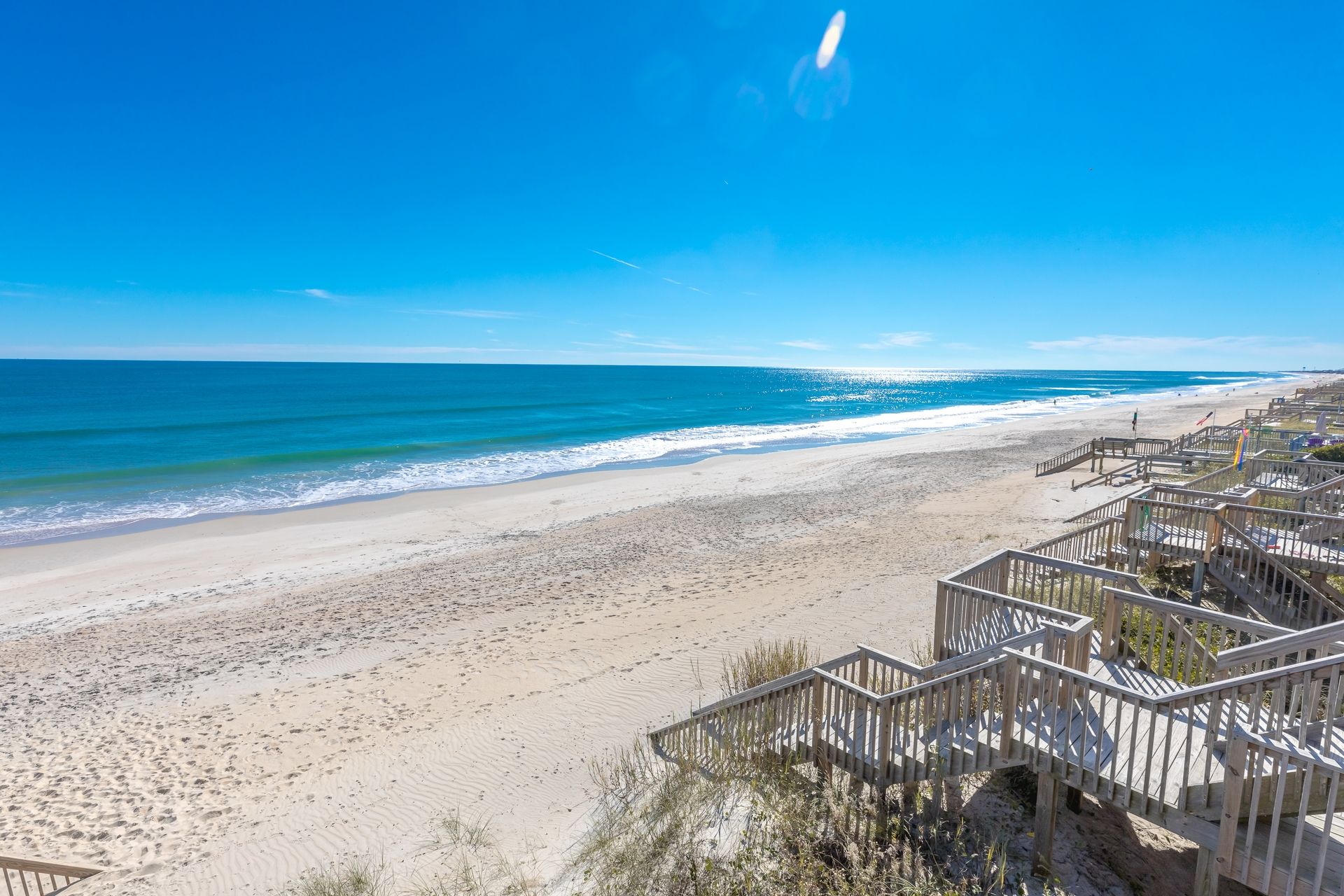 A beach with a wooden boardwalk leading to a building with multiple levels.