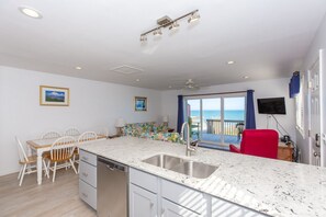 A modern kitchen with a dishwasher, a dining area with chairs, and a view of the sea through a large window.