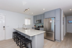 A modern kitchen with a central island, stainless steel appliances, and bar stools.