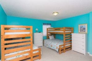 A room with two bunk beds, a white dresser, a lamp, and a framed picture on the wall.