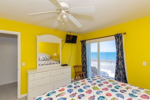 A bedroom with a bed, dresser, ceiling fan, and a view of the ocean through a window. - Fins To The Right- Oceanfront 3 Bedroom (Surf City)
