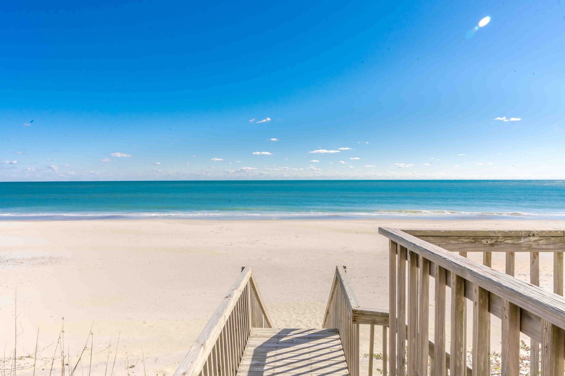A wooden boardwalk leading to a sandy beach with a clear blue sky.