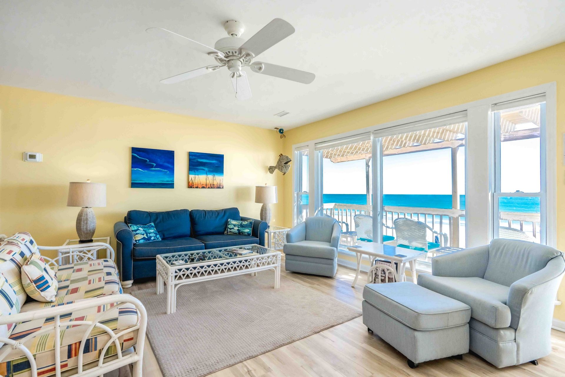 A room with a ceiling fan, a sofa, a chair, a small table, and a view of the ocean.