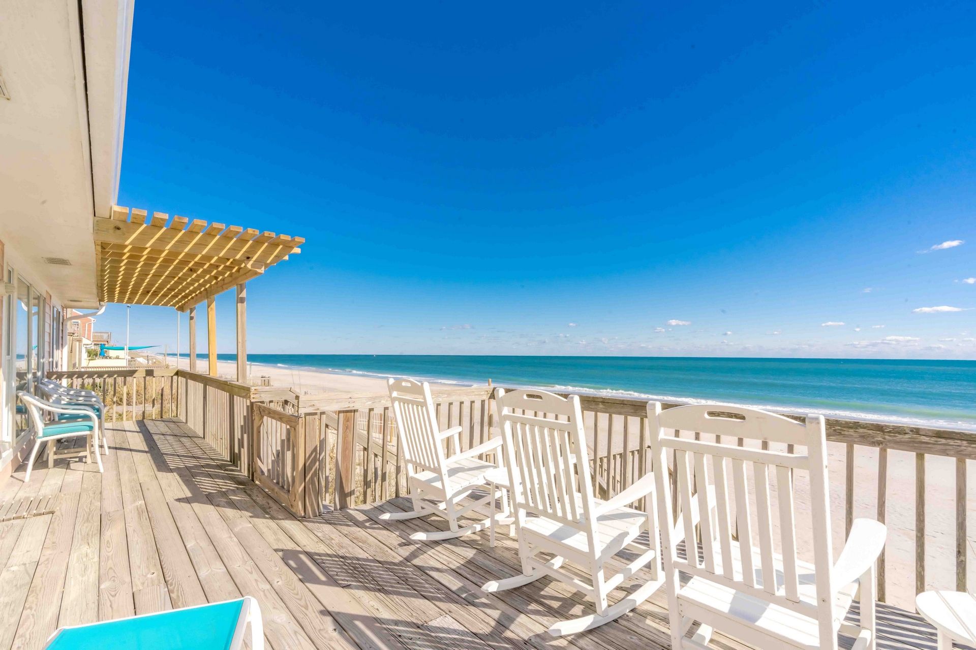 A wooden deck with white rocking chairs overlooking a beach.
