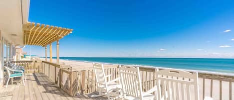 A wooden deck with white rocking chairs overlooking a beach.
