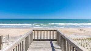 A wooden boardwalk leading to a beach with waves, clear sky, and sandy shore. - Our Heels in the Sand, a spacious 4-bedroom oceanfront home (Surf City)
