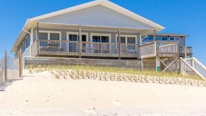 A beachfront house with a balcony, a staircase, and a sandy beach in the foreground. - Our Heels in the Sand, a spacious 4-bedroom oceanfront home (Surf City)